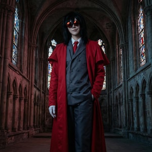Peut inclure: Une personne en costume de cosplay, portant un long manteau rouge, un costume gris, une cravate rouge et des lunettes de soleil. La personne se tient dans un bâtiment de style gothique avec des vitraux. Le costume est un cosplay du personnage de l'anime Hellsing.