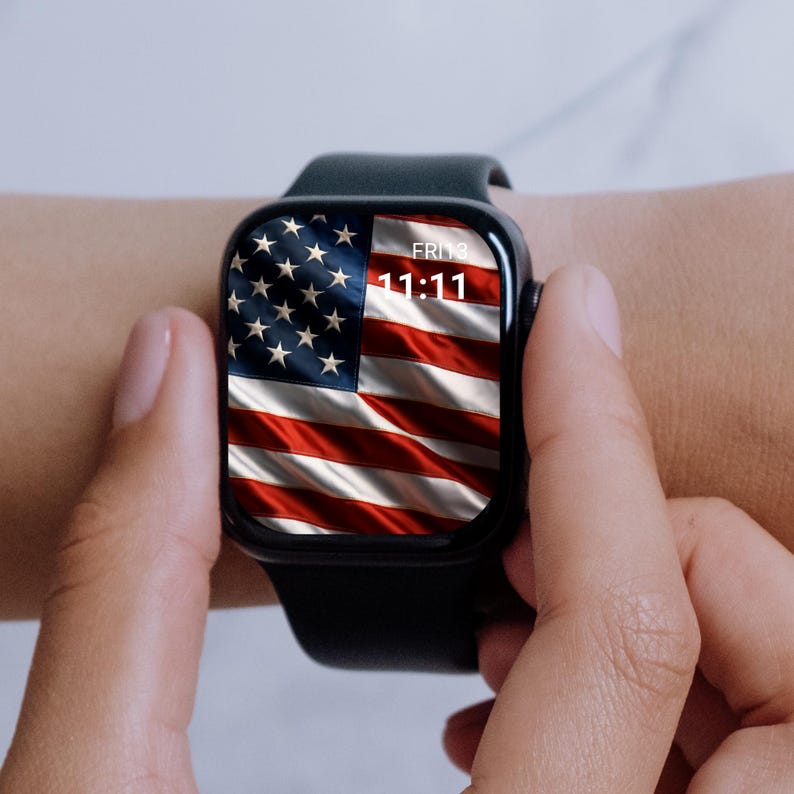 May include: A black smartwatch displaying the American flag on its screen. The time reads 11:11 on Friday. The watch is worn on a wrist, with the band appearing dark green. The watch face shows the stars and stripes of the US flag.