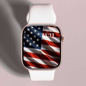 May include: A gold-colored smartwatch with a white band displays the American flag on its screen. The time is 11:11 on Friday. The watch is set against a soft pink background.