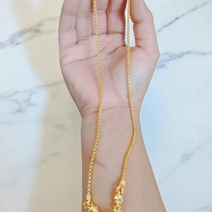 May include: A gold-colored necklace with a heart-shaped pendant and a small, round charm. The necklace is held in a hand, showcasing its intricate design and delicate chain. The pendant has a textured surface.