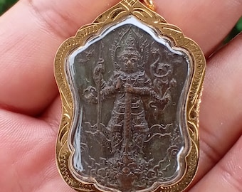 May include: A gold-colored pendant with a detailed, dark-toned figure inside a clear protective layer. The pendant has an ornate, decorative frame and a small loop for a chain.
