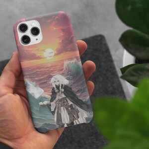 Könnte beinhalten: Handyhülle mit einer Anime-Illustration eines Charakters vor einem Sonnenuntergang über dem Meer. Das Kunstwerk verwendet Rosa-, Orange- und Blautöne. Die Hülle hat eine glänzende Oberfläche und einen Kameraausschnitt.