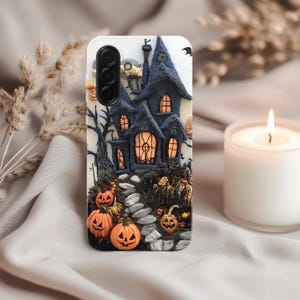 Puede incluir: Funda de teléfono blanca con una escena de Halloween esculpida en 3D. El diseño incluye una casa azul oscura con ventanas naranjas, calabazas y un camino de piedra. Una vela encendida en el fondo.