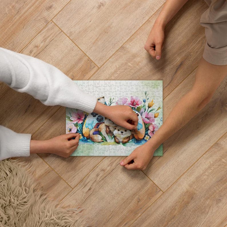 May include: A completed jigsaw puzzle featuring a watercolor illustration of a teddy bear with floral accents. The puzzle has a light green background and is surrounded by pink and blue flowers. Two people are working on the puzzle.