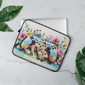 May include: Laptop sleeve with a watercolour design of otters, video game controllers, and flowers. The sleeve has a black zip and a white background. The otters are brown and the controllers are blue and orange.