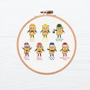 Op de afbeelding: Een ronde houten borduurring met een kruissteekpatroon van zeven antropomorfe gele knoedels met diverse hoeden en accessoires. De tekstlabels bevatten Bacon Burt, Cheese Chester, Jalapeno Hannah, Oliver Onion, Pizza Penny, Potato Pete en Sauerkraut Saul.