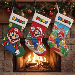 Puede incluir: Tres calcetines navideños con personajes de Mario. El izquierdo es verde con Mario, el central es rojo con Mario en una escena invernal y el derecho es azul con Mario en un paisaje. Cada uno tiene un puño blanco con la palabra Name impresa.