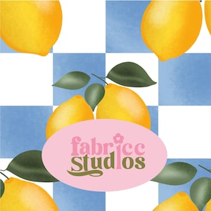 Pode incluir: Um padrão repetitivo de limões amarelo-brilhante com folhas verde-escuras sobre um fundo xadrez azul-claro e branco. Um oval rosa no centro exibe o texto fabricc studios numa fonte estilizada de cor verde-escura.