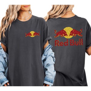 a woman wearing a grey t-shirt with a graphic design of two red bulls and the text "Red Bull" on the back.