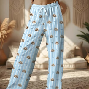May include: Light blue pyjama trousers with a vertical stripe pattern and repeating images of a dog's face and bows. The trousers have a drawstring waist.