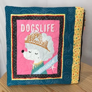 May include: Square quilted pillow with a pink center featuring a white poodle wearing a gold crown and the text "DOGSLIFE". The pillow has a teal border with white floral stitching, a black and white polka dot border, and a yellow polka dot edge.