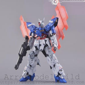 May include: A detailed robot model in blue, white, red, and grey. It features large red wings and a black gun. The robot is posed with legs apart. The text "ArrowModelBuild" is visible. The model is a detailed representation.