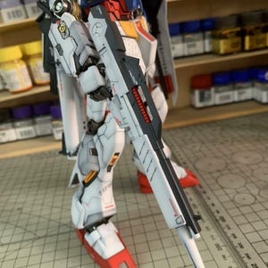 K&ouml;nnte beinhalten: Detailliertes Modell eines Roboters, haupts&auml;chlich wei&szlig; mit roten, blauen und gelben Akzenten. Der Roboter h&auml;lt eine gro&szlig;e, schwarz-wei&szlig;e Waffe. Das Modell ist teilweise montiert und zeigt komplizierte mechanische Details. Der Text "AeroModel Build" ist sichtbar.