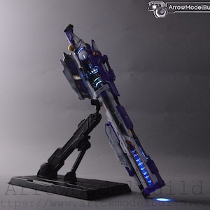 Könnte beinhalten: Ein futuristisches Modell einer Waffe in Lila, Weiß und Grau, beleuchtet mit blauen LED-Leuchten. Das Modell ist auf einem schwarzen Ständer montiert. Der Text "ArrowModelBuild" ist in der oberen rechten Ecke sichtbar.