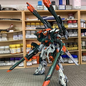 May include: A detailed model of a mech warrior, featuring a color scheme of white, green, and orange. The model has multiple weapons and is posed on a cutting mat. The text "ArrowModelBuild" is visible.