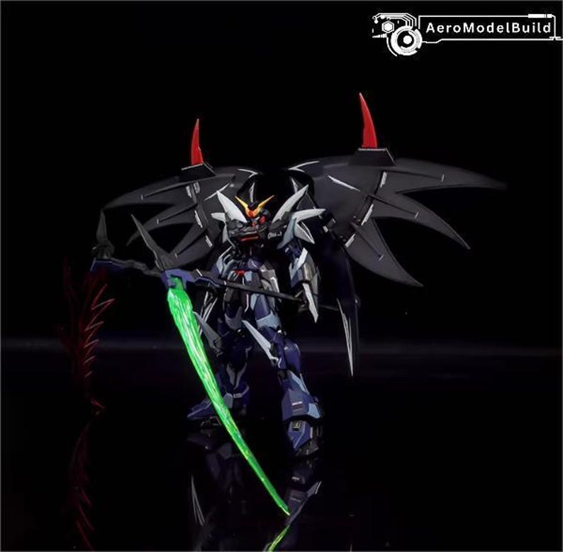 Puede incluir: Modelo detallado de un robot Gundam, con una combinaci&oacute;n de colores azul oscuro y blanco, alas negras y detalles rojos. El robot sostiene un arma de energ&iacute;a verde, sobre un fondo negro.