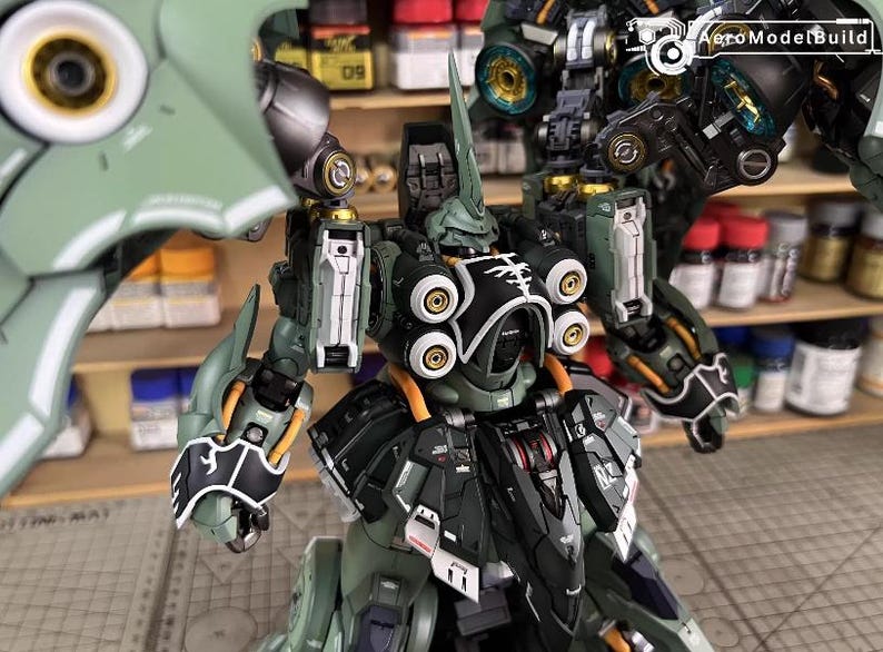 May include: A detailed model of a green and black mecha robot with intricate mechanical details. The model features multiple articulated joints, circular accents, and a prominent horn-like structure on its head. The AeroModelBuild logo is visible in the background.