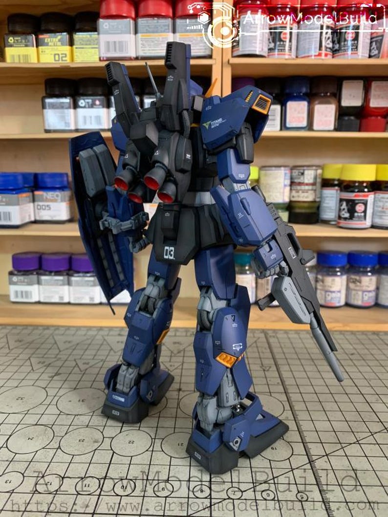May include: A detailed model kit of a mecha robot, primarily in navy blue and black with orange and gray accents. The robot is posed with a gun and shield, showcasing intricate mechanical details. The model is on a grid surface.