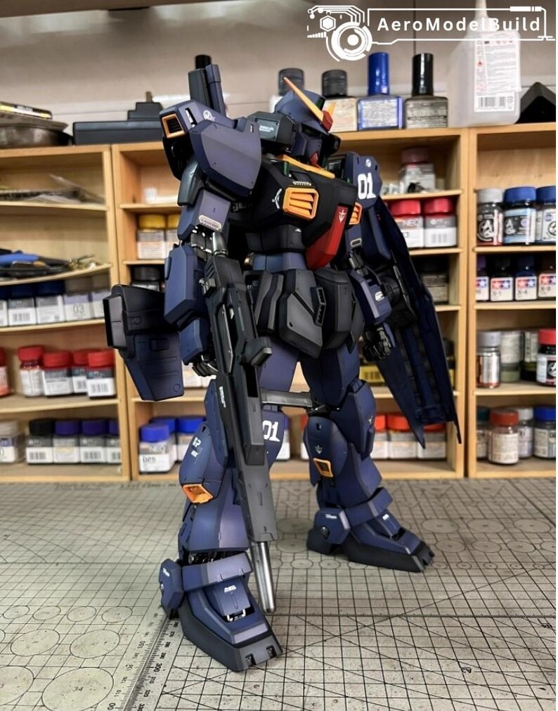Pu&ograve; includere: Un modello dettagliato di un robot meccanico blu scuro e nero con accenti arancioni e rossi. Il robot tiene in mano una grossa pistola e ha il numero "01" stampato sulla gamba e sul petto. Il testo "AeroModelBuild" &egrave; visibile in alto a destra.