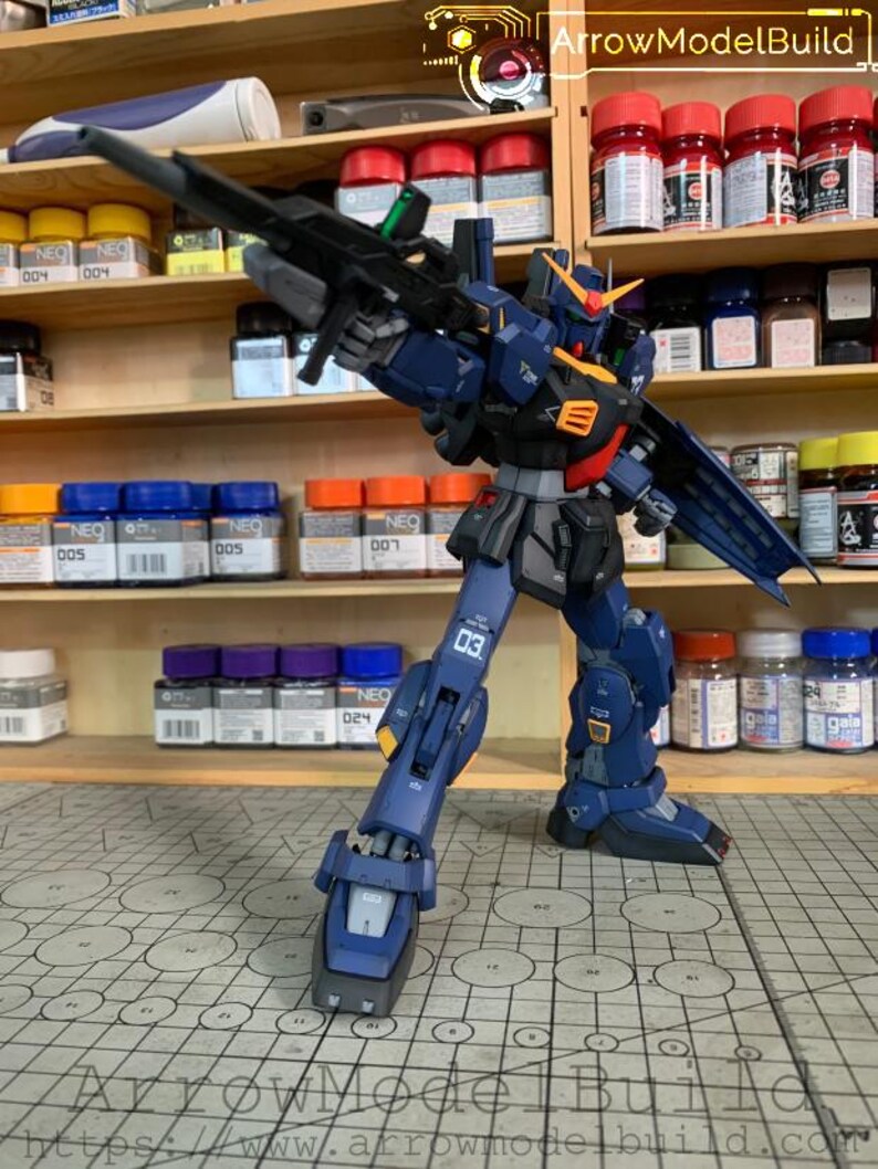 May include: A detailed, poseable model kit of a mecha robot, primarily navy blue with orange and yellow accents. The robot is holding a large black rifle and is standing on a grid-patterned surface. The model is surrounded by shelves of paint jars.