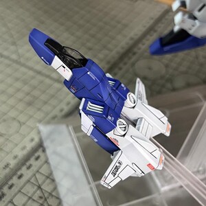 May include: A detailed model aircraft in blue and white, showcasing panel lines and markings. The model includes a cockpit and wing-like structures. The text "DOA 27" is visible. The AeroModelBuild logo is in the background.
