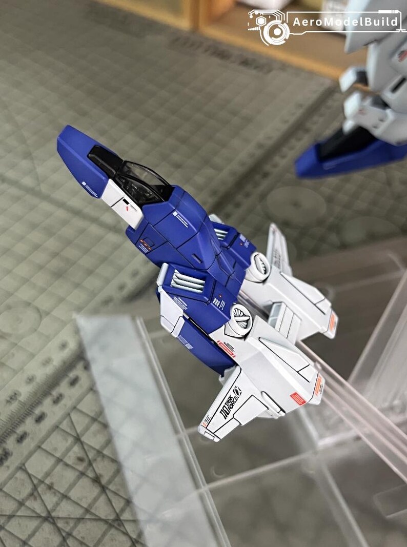 May include: A detailed model aircraft in blue and white, showcasing panel lines and markings. The model includes a cockpit and wing-like structures. The text "DOA 27" is visible. The AeroModelBuild logo is in the background.