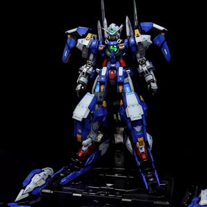 May include: A detailed model of a futuristic robot, primarily blue and white, with red and yellow accents. The robot is standing on a black base. The image includes the text "AeroModelBuild" and "alexshop".