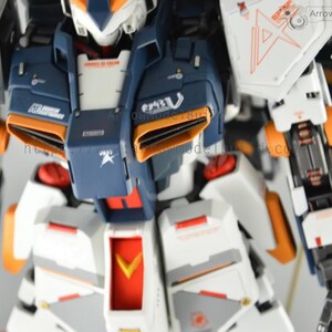 May include: Close-up of a detailed, articulated robot model. The model features a color scheme of white, navy blue, and orange. The robot has intricate mechanical details, including panels, vents, and markings. The model is a collectible item.