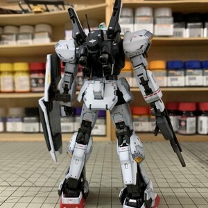 Pode incluir: Um modelo de rob&ocirc; detalhado e montado, principalmente branco com detalhes cinza e preto. O rob&ocirc; apresenta membros articulados, um escudo e uma arma. O modelo est&aacute; situado em um fundo de potes de tinta e prateleiras, sugerindo um tema de hobby ou modelagem.