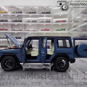 May include: A blue model SUV with the hood and doors open, revealing a detailed interior. The model has black wheels and a spare tire on the back. The text "ArrowModelBuild" and a website address are visible.
