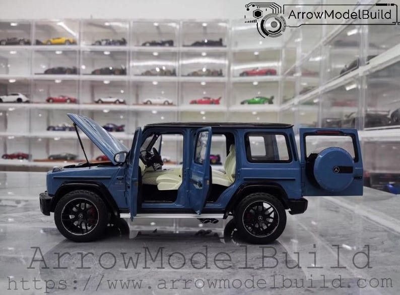 May include: A blue model SUV with the hood and doors open, revealing a detailed interior. The model has black wheels and a spare tire on the back. The text "ArrowModelBuild" and a website address are visible.
