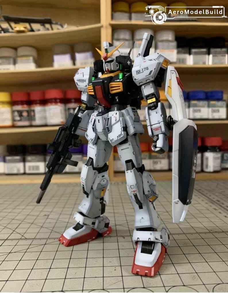 Pode incluir: Modelo detalhado de um rob&ocirc; branco, cinza, preto e vermelho com um rifle e um escudo. O rob&ocirc; tem pain&eacute;is intrincados e est&aacute; posicionado em uma superf&iacute;cie de grade. O modelo tem o texto "RX-178" e "AeroModelBuild".