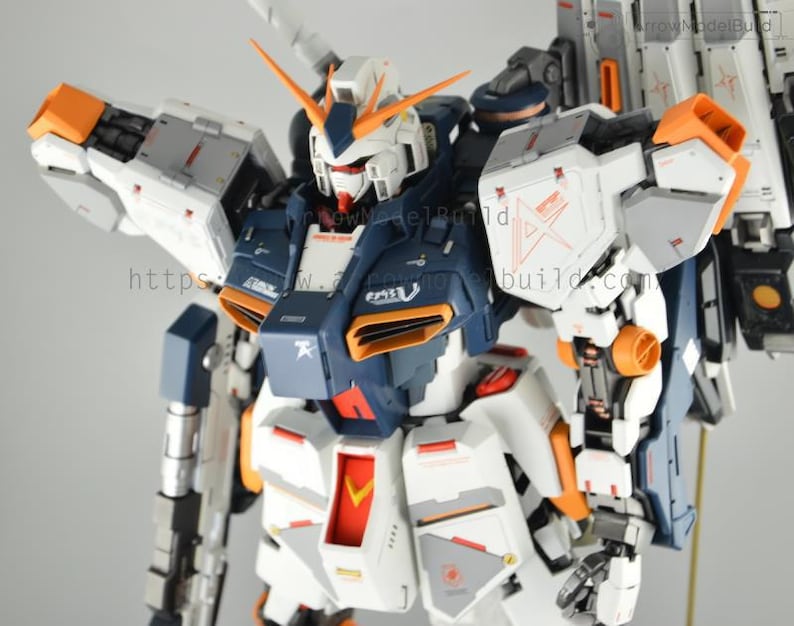May include: A detailed model of a mecha robot, featuring a color scheme of white, navy blue, and orange. The robot has intricate paneling and design elements, with visible text on its surface. The overall aesthetic suggests a futuristic or science fiction theme.