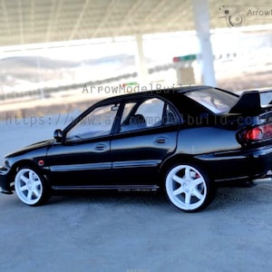 Könnte beinhalten: Ein schwarzes Modellauto mit weißen Rädern und einem Heckspoiler. Das Auto hat ein schlankes Design und steht auf einer grauen Oberfläche. Der Text "ArrowModelBuild" und eine Website-Adresse sind sichtbar.