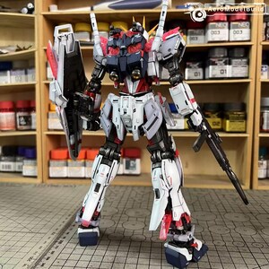 May include: A detailed model of a robot with a white, red, and black color scheme. The robot has a shield, a rifle, and multiple antennas. The model is standing on a surface with a ruler and is in front of a shelf with paint supplies.