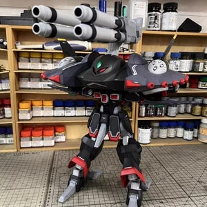 May include: A detailed model of a black, gray, and red mech with multiple missile launchers. The model has articulated legs and arms, with red accents on the feet and shoulders. The model is on a cutting mat with a grid pattern.
