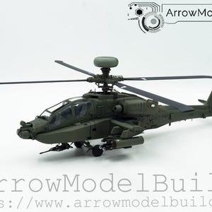 May include: A detailed model of an Apache military helicopter, painted in olive drab green. The model features intricate details, including rotors, weapons, and the "ArrowModelBuild" logo. The model is displayed on a white background.
