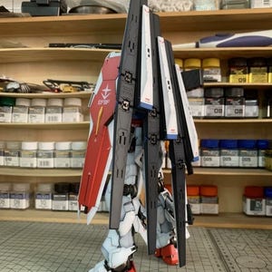 K&ouml;nnte beinhalten: Ein teilweise zusammengebauter Modellbausatz eines Mecha-Roboters mit roten, wei&szlig;en, schwarzen und blauen Akzenten. Das Modell weist komplizierte Details wie Paneele, Fl&uuml;gel und Gelenke auf. Der Text "EFSF" ist auf dem roten Schild sichtbar.