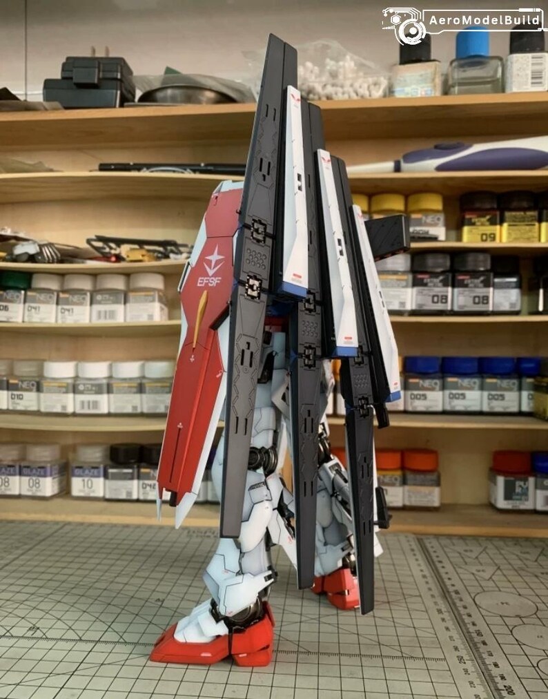 K&ouml;nnte beinhalten: Ein teilweise zusammengebauter Modellbausatz eines Mecha-Roboters mit roten, wei&szlig;en, schwarzen und blauen Akzenten. Das Modell weist komplizierte Details wie Paneele, Fl&uuml;gel und Gelenke auf. Der Text "EFSF" ist auf dem roten Schild sichtbar.