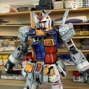 K&ouml;nnte beinhalten: Ein detailliertes Modell eines Gundam-Roboters mit einem Farbschema aus Wei&szlig;, Blau, Rot und Gelb. Der Roboter hat bewegliche Gliedma&szlig;en und komplizierte Linien. Das Modell wird vor Regalen mit Malutensilien ausgestellt.