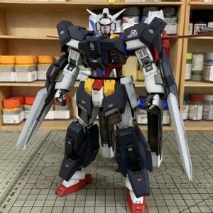 Puede incluir: Modelo detallado de un robot mecha, con una combinaci&oacute;n de colores azul marino, blanco, rojo y amarillo. El robot tiene extremidades grandes y articuladas y est&aacute; equipado con dos grandes cuchillas plateadas. El modelo est&aacute; sobre una superficie cuadriculada.