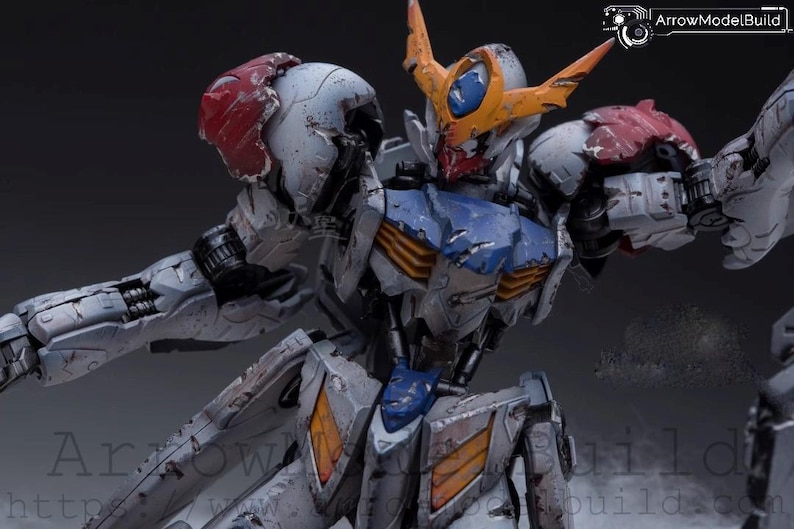 May include: Detailed model of a battle-worn robot with a white, blue, orange, and red color scheme. The robot has intricate mechanical details, visible damage, and a dynamic pose. The image includes the text "ArrowModelBuild".