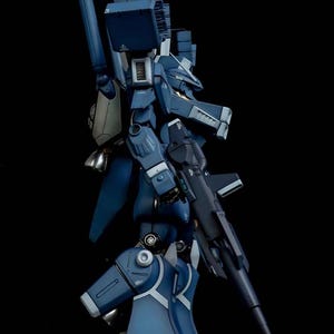 May include: A detailed side view of a dark blue model robot with a gun. The robot has multiple panels, joints, and a large backpack. The AeroModelBuild logo is in the top right corner.
