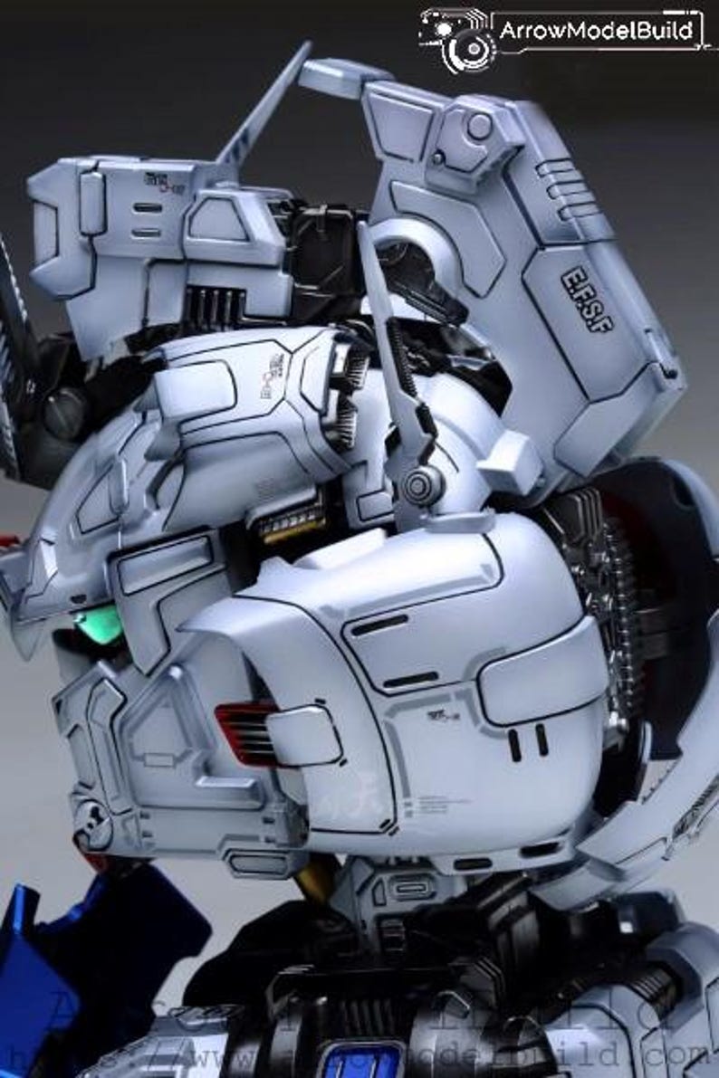 Może przedstawiać: Szczeg&oacute;łowe zbliżenie białego i szarego modelu robota ze skomplikowanymi detalami mechanicznymi. Zawiera panele, stawy i napis "E.F.S.F." na ramieniu. Model ma futurystyczny design.