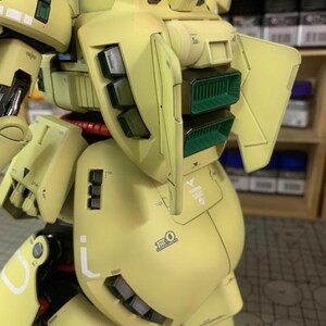 May include: A detailed, assembled model kit of a yellow and green mech robot. The model features intricate panel lines, vents, and markings. The robot has a rounded body with angular armor plates and a complex design.