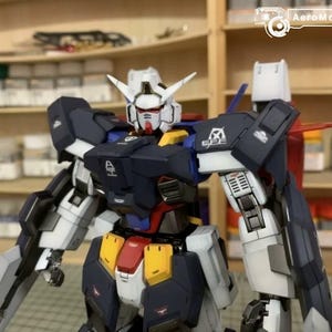 Puede incluir: Modelo detallado de un robot Gundam, con cabeza blanca y detalles rojos, torso azul marino y extremidades blancas y grises. El modelo presenta detalles amarillos y rojos, con componentes mec&aacute;nicos visibles.