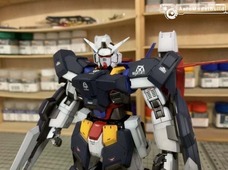 Puede incluir: Modelo detallado de un robot Gundam, con cabeza blanca y detalles rojos, torso azul marino y extremidades blancas y grises. El modelo presenta detalles amarillos y rojos, con componentes mec&aacute;nicos visibles.