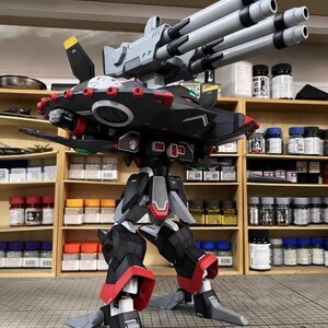 May include: AeroModelBuild model of a black, red, and gray robot with multiple gray gun barrels. The robot has articulated legs and arms, with red accents on the joints. The model is displayed on a gray surface.