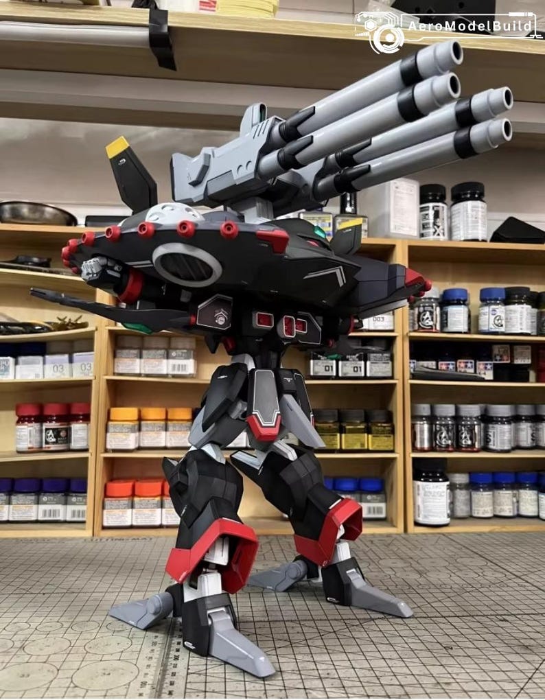 May include: AeroModelBuild model of a black, red, and gray robot with multiple gray gun barrels. The robot has articulated legs and arms, with red accents on the joints. The model is displayed on a gray surface.