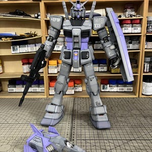 May include: A detailed model of a gray and purple robot with a matching aircraft. The robot has the text "EFSF" and "WB 103" printed on it. The aircraft is gray and purple with the text "ArrowModelBuild" on the bottom.